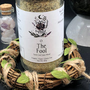 Spice blend labeled 'The Fool' from Dahlia's Enchanted Kitchen on a decorative stand with crystals in the background.
