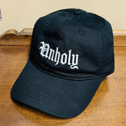 Black cap with 'Unholy' text on a wooden surface