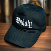 Black cap with 'Unholy' text on a wooden surface