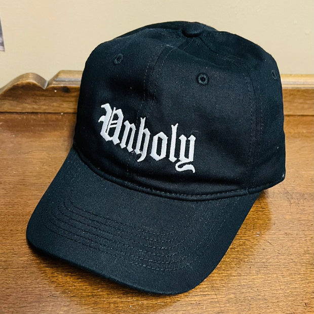 Black cap with 'Unholy' text on a wooden surface