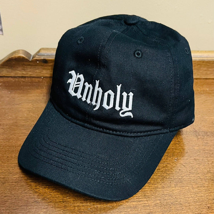 Black cap with 'Unholy' text on a wooden surface