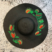 Black straw hat with red and green floral embroidery on a textured surface