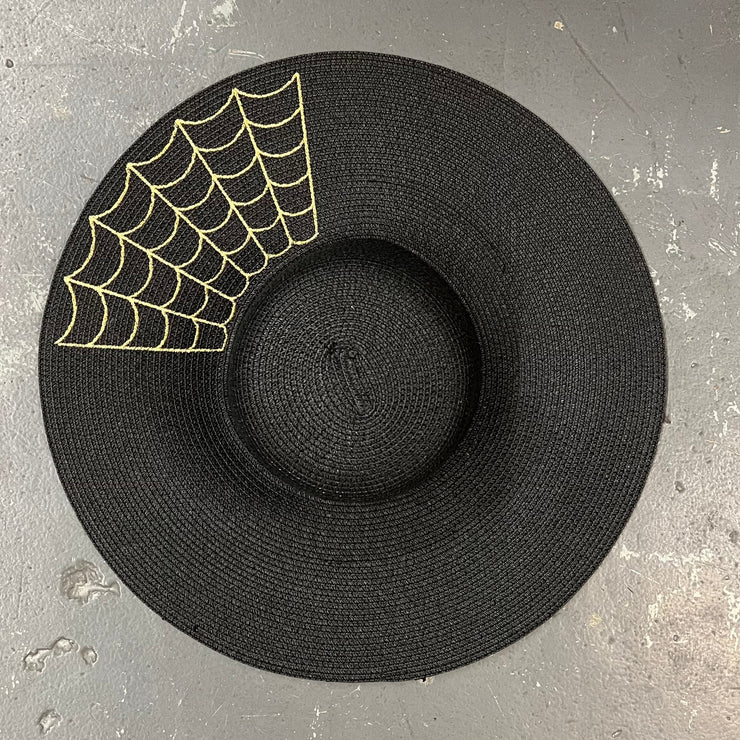Black straw hat with gold spider web design on a gray surface