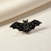 Bat shaped enamel pin with moon and star detailing on its wings on a light background