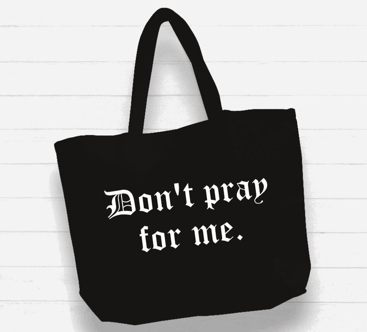 Black tote bag with 'Don't pray for me' text on a white wooden background