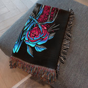 Intriguing Crow and Flowers Woven Throw Blanket with a crow in shades of black and blue against a dramatic background of magenta splashes and abstract shapes. Perfect for wall decoration, a cozy throw, or a unique picnic spread.