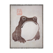 Frog by Matsumoto Hoji Woven Throw Blanket from Meika Gafu, 1814, featuring a sad-faced frog in black ink beneath red calligraphy. This Zen-inspired design was common during the Japanese Edo period, representing a pure and natural life.