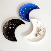 The Bleak Boutique Crescent Moon Ceramic Jewelry Valet Dishes—black, blue, and white with gold stars—are arranged in a circular pattern as charming trinket holders on a light surface.