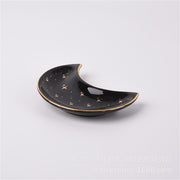 The Crescent Moon Ceramic Jewelry Valet Dish by Bleak Boutique features gold star patterns and a gold rim—ideal for holding trinkets or jewelry—and is shown on a plain white background.