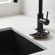 The Crescent Moon Ceramic Jewelry Valet Dish by Bleak Boutique, adorned with gold star patterns, elegantly holds a silver ring with a large clear gemstone, making it a stylish jewelry caddy on a white surface.