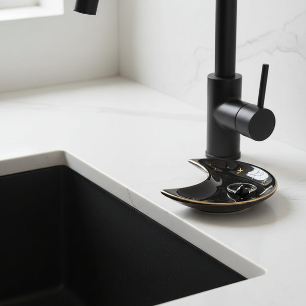 The Crescent Moon Ceramic Jewelry Valet Dish by Bleak Boutique, adorned with gold star patterns, elegantly holds a silver ring with a large clear gemstone, making it a stylish jewelry caddy on a white surface.