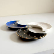 The Bleak Boutique Crescent Moon Ceramic Jewelry Valet Dishes in black, blue, and white feature gold star accents and are arranged on a light surface. Ideal as a jewelry caddy or trinket holder.