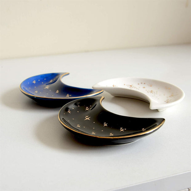 The Bleak Boutique Crescent Moon Ceramic Jewelry Valet Dishes in black, blue, and white feature gold star accents and are arranged on a light surface. Ideal as a jewelry caddy or trinket holder.