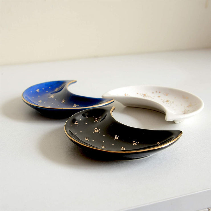The Bleak Boutique Crescent Moon Ceramic Jewelry Valet Dishes in black, blue, and white feature gold star accents and are arranged on a light surface. Ideal as a jewelry caddy or trinket holder.