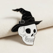 The Skull in Witch Hat Enamel Lapel Pin by Bleak Boutique features a smiling cartoon skull with empty eye sockets, a witch hat, and pentagram—perfect as a spooky accessory or pin.