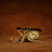 Small brass octopus figurine holding a pen in its raised tentacles.